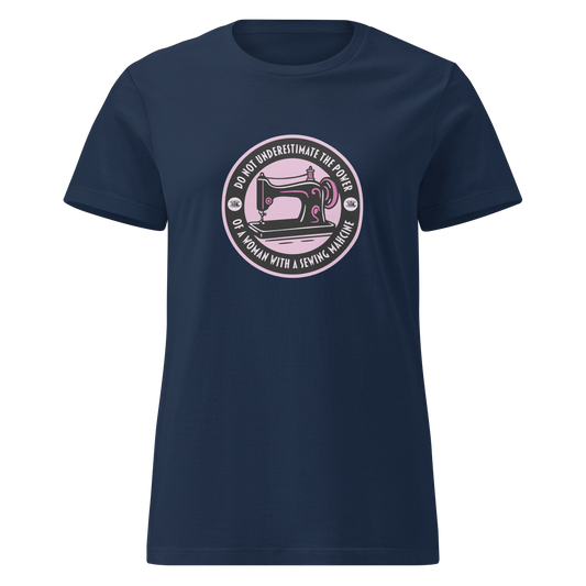 Tummansininen naisten soft-style huumoripaita, jonka keskellä on musta-pinkki painatus ompelukoneesta. Kehällä valkoinen teksti “Do not underestimate the power of a woman with a sewing machine” – kielletään kaikki
