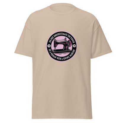 Beige unisex huumoripaita, jonka keskellä pinkki ympyräpainatus. Kuvassa ompelukone, kehällä mustalla teksti “Do not underestimate the power of a woman with a sewing machine” – kielletään kaikki
